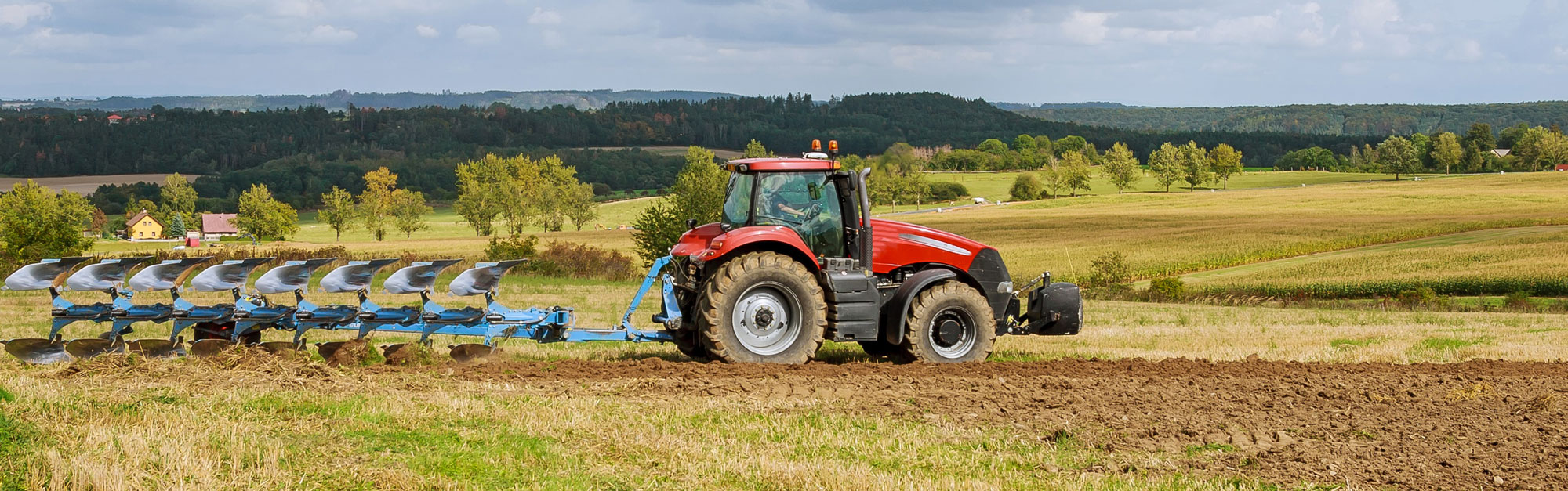 Farmer in red tractor preparing land with plow for sowing